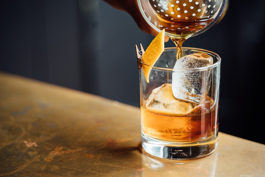 a cocktail being strained into a a glass with orange twist and ice