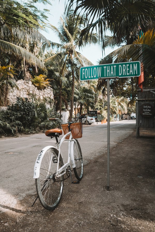 a bicycle on the side of the road, with a sign that says "follow that dream" illustrating slow travel