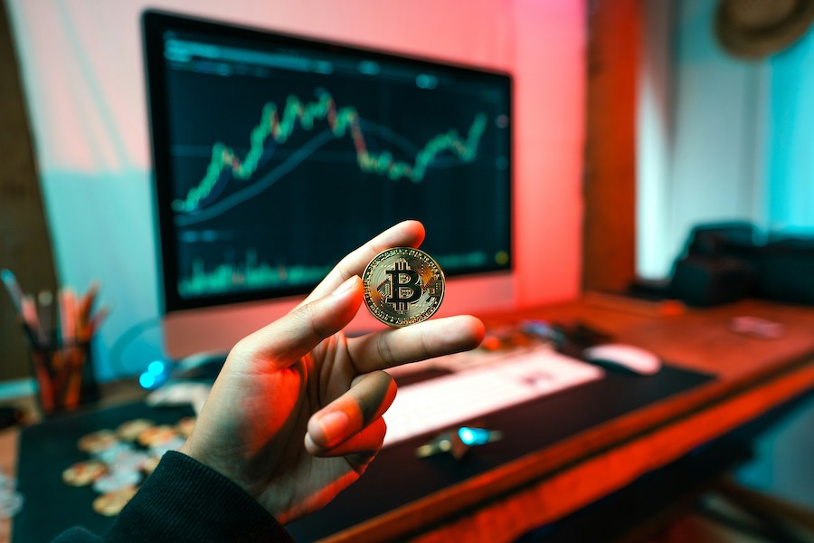 a man holding bitcoin icon with the background of a room and a led screen with cryptocurrency buy-sell screen