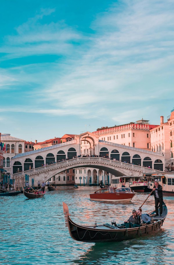 a medieval bridge with tourists on it, possibly in Venice canals, illustrating slow travel